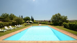 A rectangular swimming pool with a clear blue water surface, surrounded by a brick border. There are white lounge chairs aligned on the left side of the pool. - Dionisia, Capannole, Gaiole in Chianti, Siena and Chianti (Gaiole in Chianti)