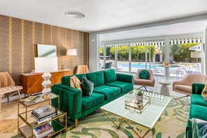 A living room with a green sofa, a glass coffee table, and a pool view.