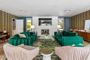 A living room with two green sofas, a glass coffee table, and a white fireplace.
