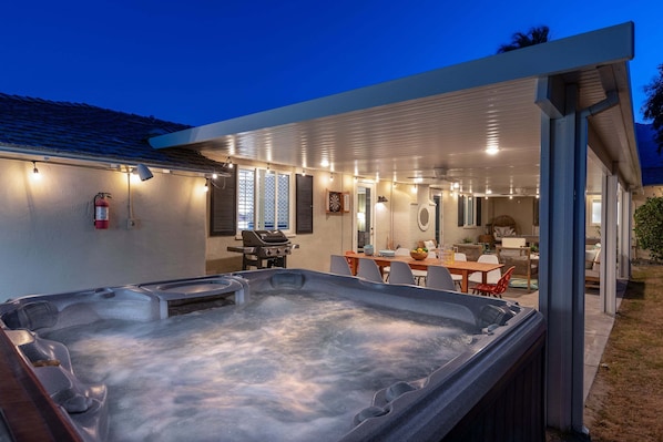 A hot tub in a covered outdoor area with a dining table and chairs, a barbecue grill, and a fire extinguisher. - Thanks for the Memory – Bob Hope Historic Estate (Palm Springs)