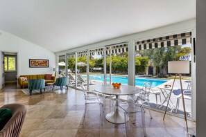 A spacious living area with a pool view, clear glass chairs, a round table, and a sofa.