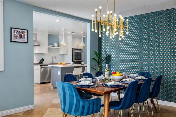 A dining area with a wooden table, blue chairs, and a chandelier. - Thanks for the Memory – Bob Hope Historic Estate (Palm Springs)