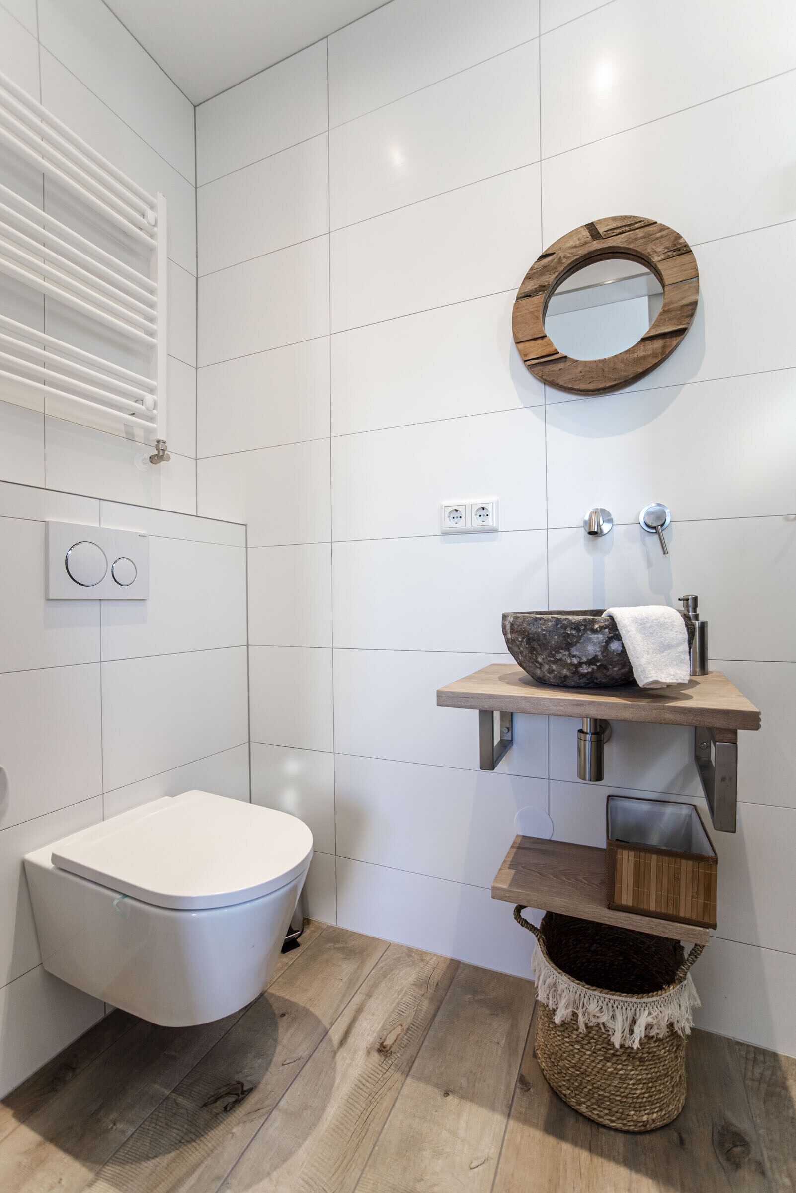 Ein modernes Badezimmer mit Toilette in Weiß, einem Holzwaschtisch mit Marmorbecken, einem runden Spiegel und einem gewebten Korb.