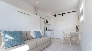 Ein modernes Wohnzimmer mit einer Couch, einem Esstisch mit Stühlen und einer Küche im Hintergrund.