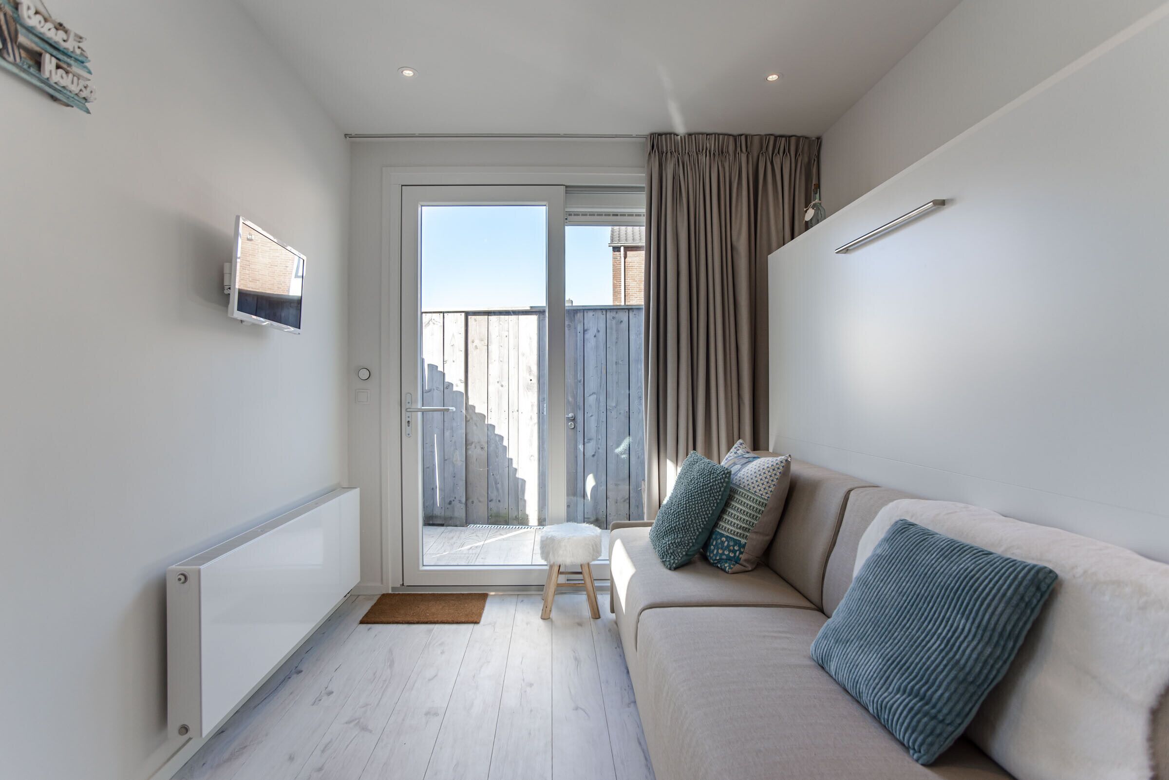 Un salon moderne avec un canapé, un petit tabouret et une porte-fenêtre coulissante donnant sur un balcon.