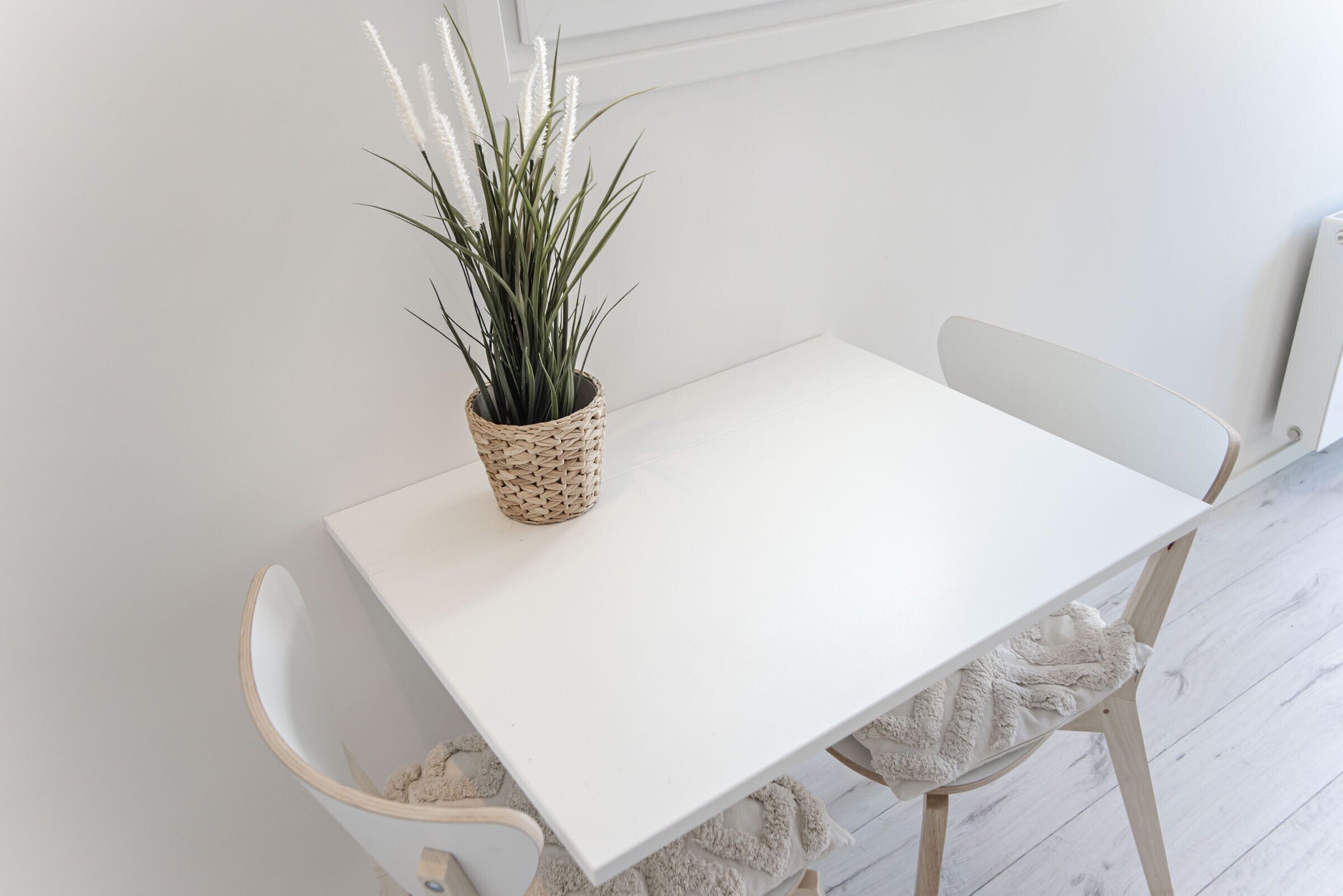 A white table with a woven plant pot, a white chair, and a white cushion.
