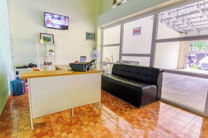 A reception area with a reception desk, a black leather couch, a large window with a view of the outside, and a television mounted on the wall. - OYO 3493 Nami House (Medan)