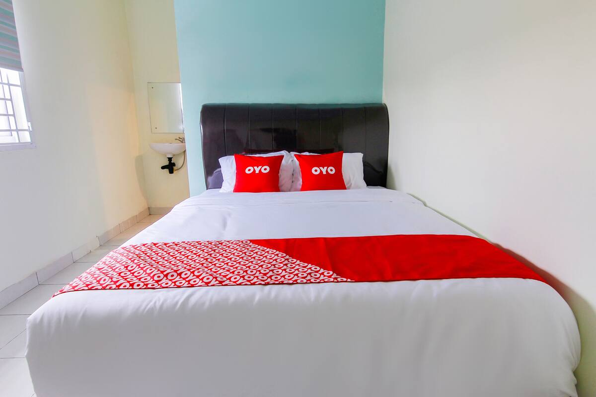 A neatly made bed with white and red bedding, a black headboard, and two red pillows with "OYO" on them.