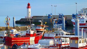 Ein Hafen mit verschiedenen Schiffen, einem Leuchtturm und einer Pier mit einer Umzäunung.