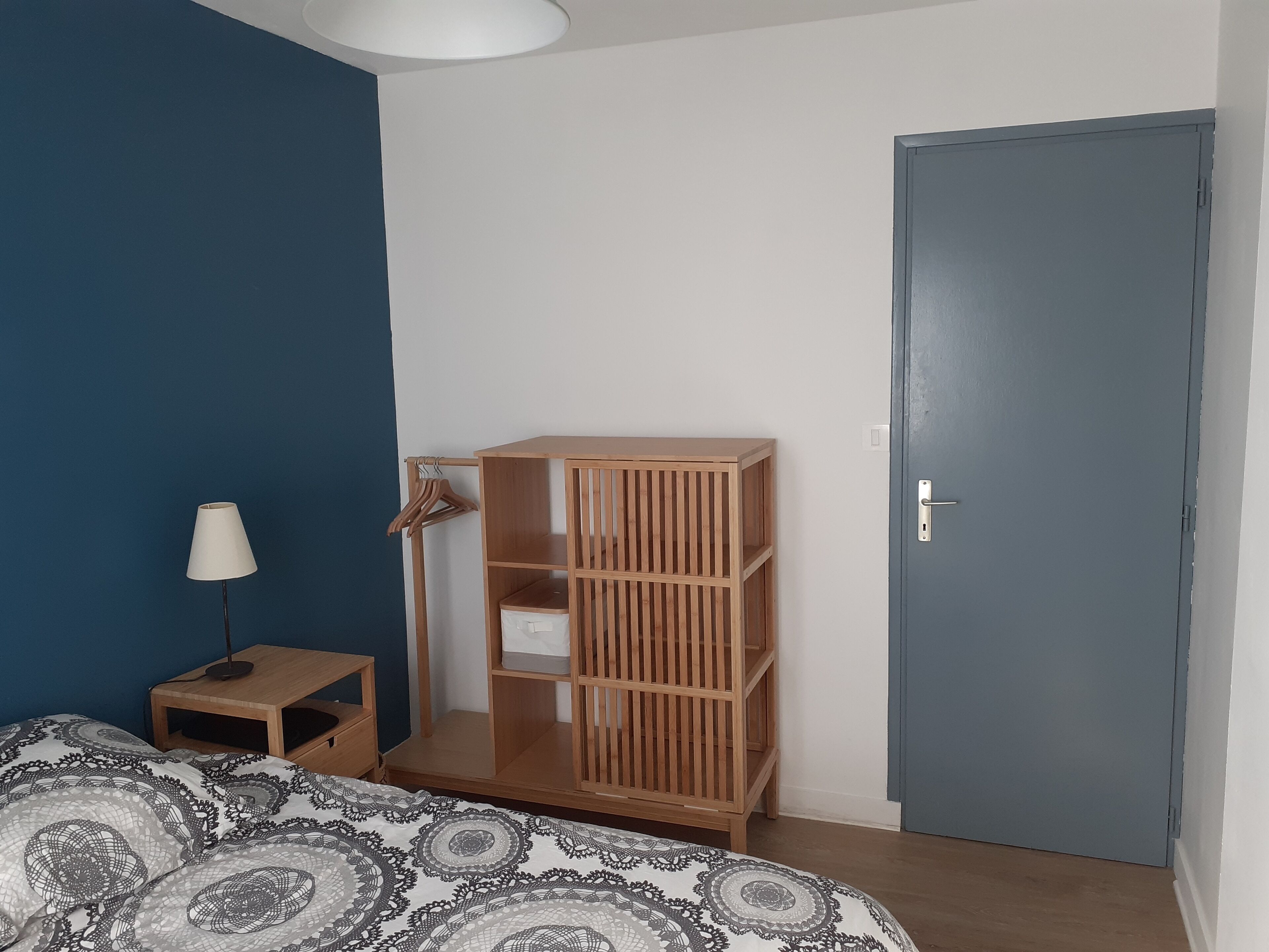 Een slaapkamer met een bed, een houten garderobe, een nachtkastje met een lamp en een deur.