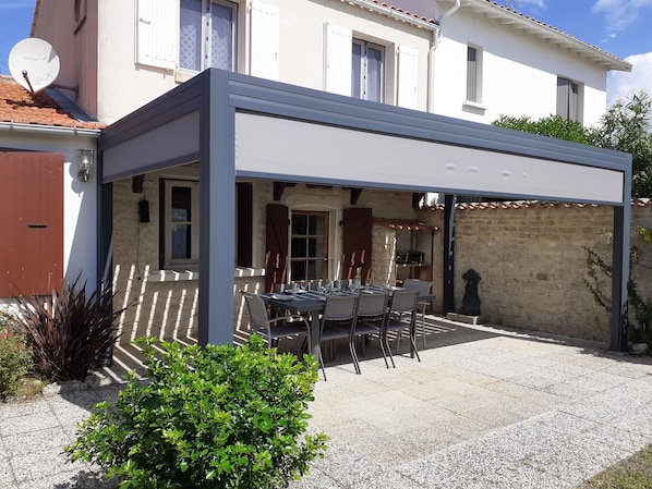 A covered outdoor dining area with a table set for four, surrounded by stone walls and a satellite dish.