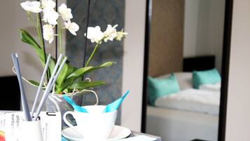 Habitación de hotel con cama, un espejo, una planta de orquídea blanca y una taza blanca con servilleta azul.