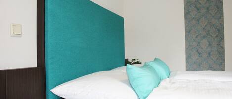 A neatly made bed with white and teal bedding, a teal headboard, and a small bedside table with a teal candle.