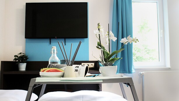 Une chambre d’hôtel avec un lit, une table de chevet sur laquelle se trouvent une bouteille, une tasse et une plante.
