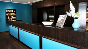 Un comptoir d’accueil avec un revêtement en bois foncé, un mur d’accent bleu et un vase blanc orné de fleurs.