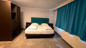 Een hotelkamer met een bed, een kledingkast, een nachtkastje en een raam met gordijnen.