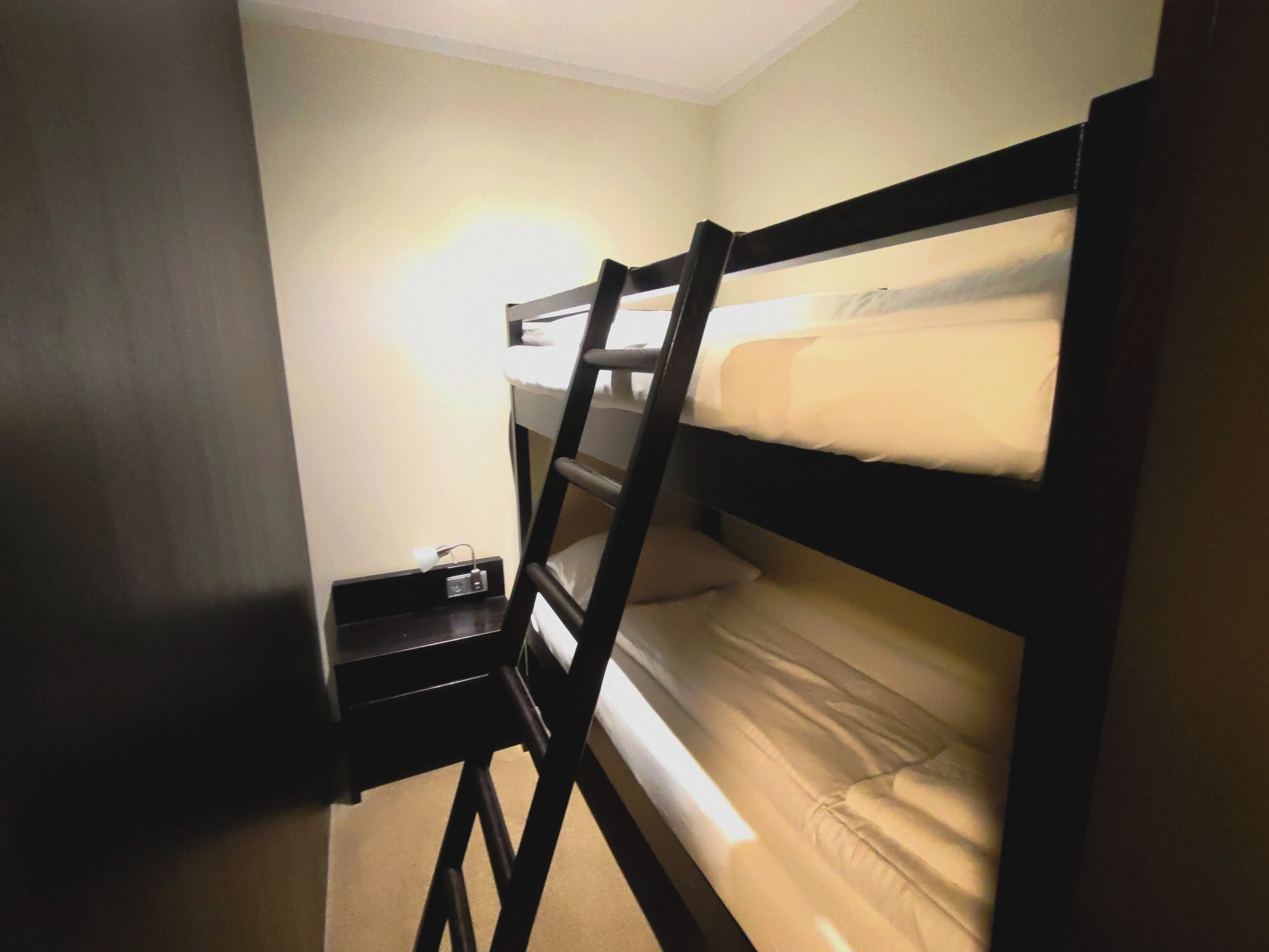 Ein Stockbett mit einer Leiter, ein Nachttisch mit einer Lampe und eine Steckdose.