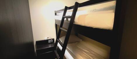 Una cama litera con escalera, una mesita de noche con lámpara y un enchufe en la pared.