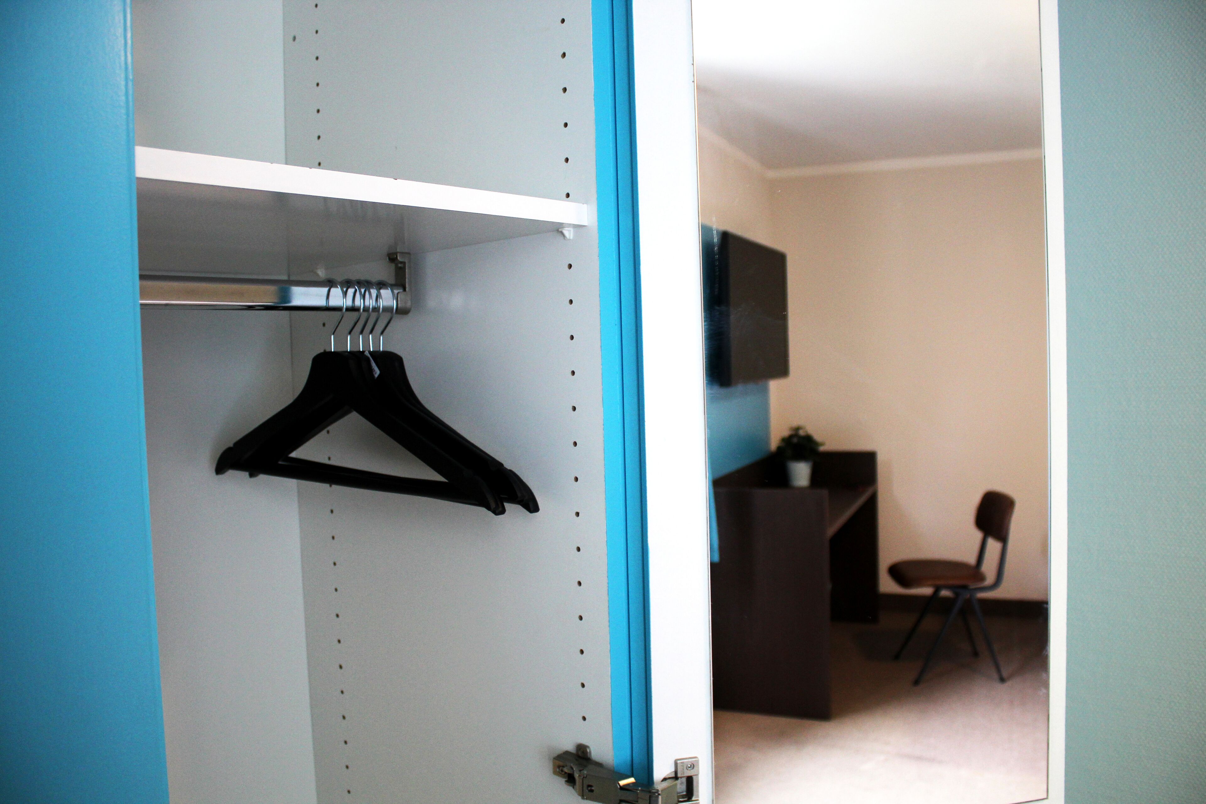 A room with a wardrobe, a chair, and a television.