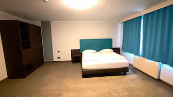 Una habitación de hotel con cama, mesita de noche, armario y ventana con cortinas.
