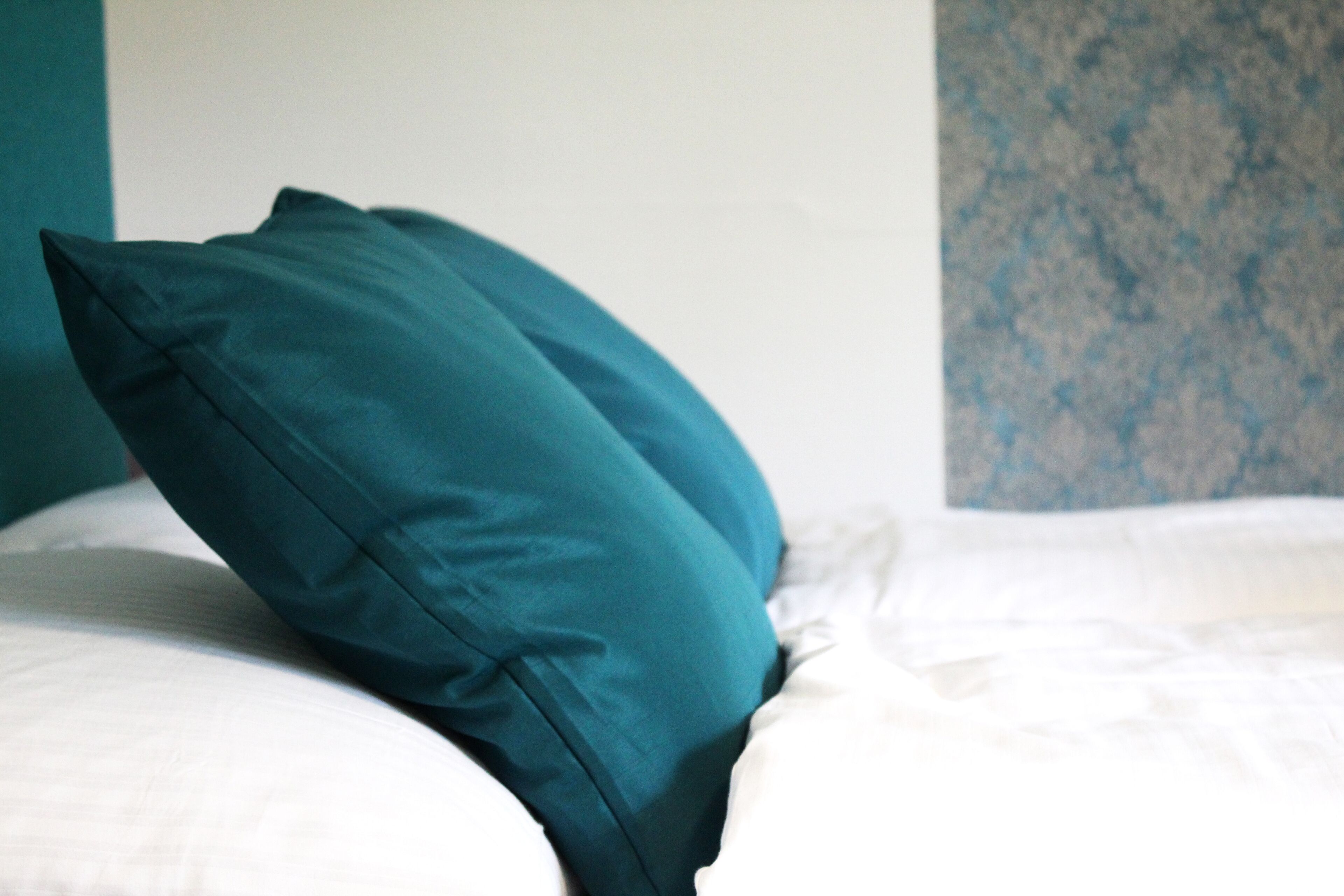 A bed with teal pillows and white bedding.