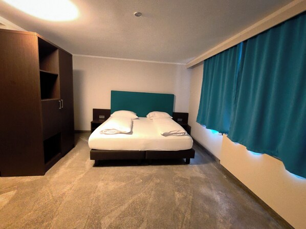 Una habitación de hotel con una cama, un armario y una cortina.