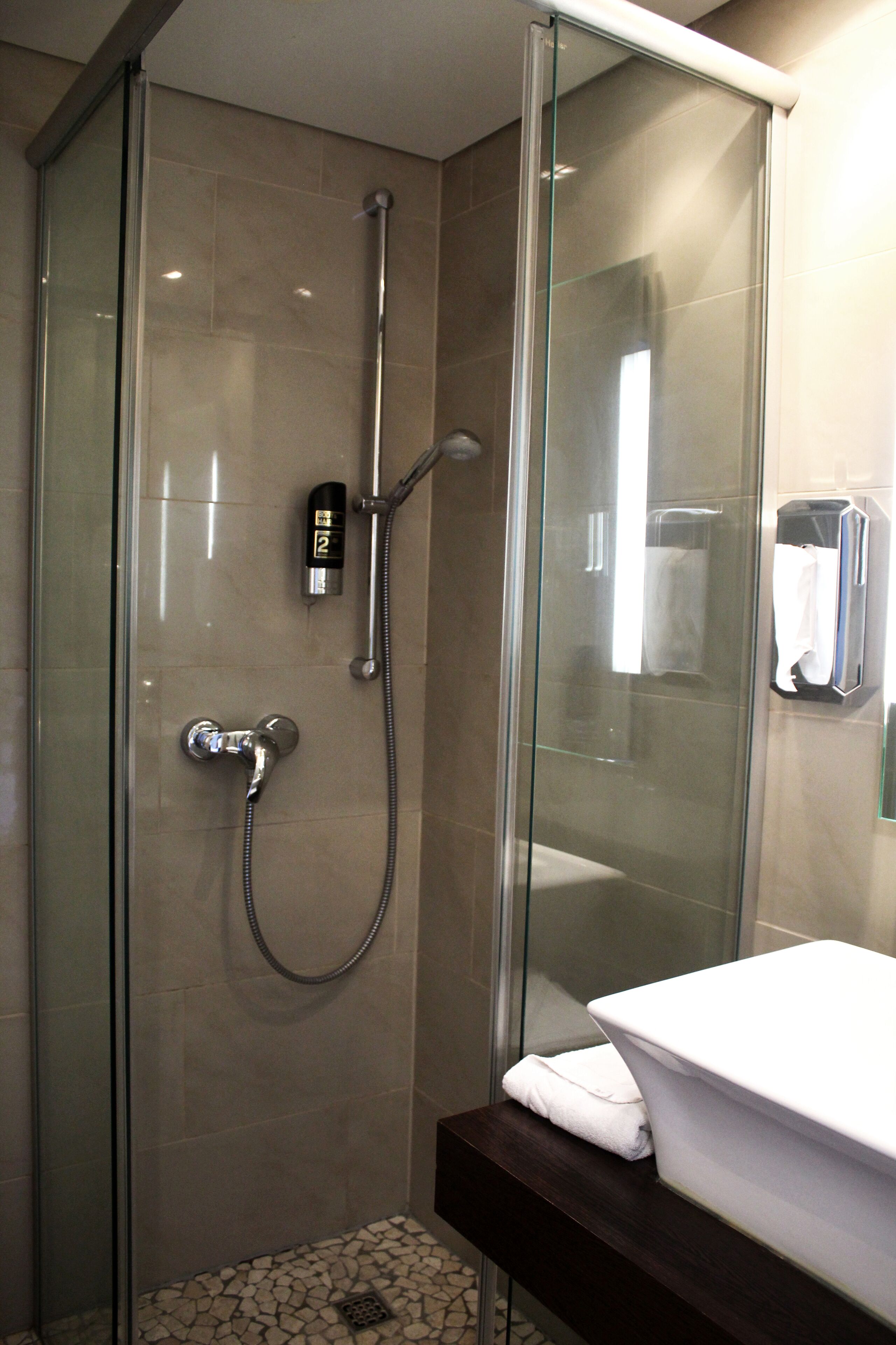 A glass-enclosed shower with a handheld showerhead and a wall-mounted faucet.