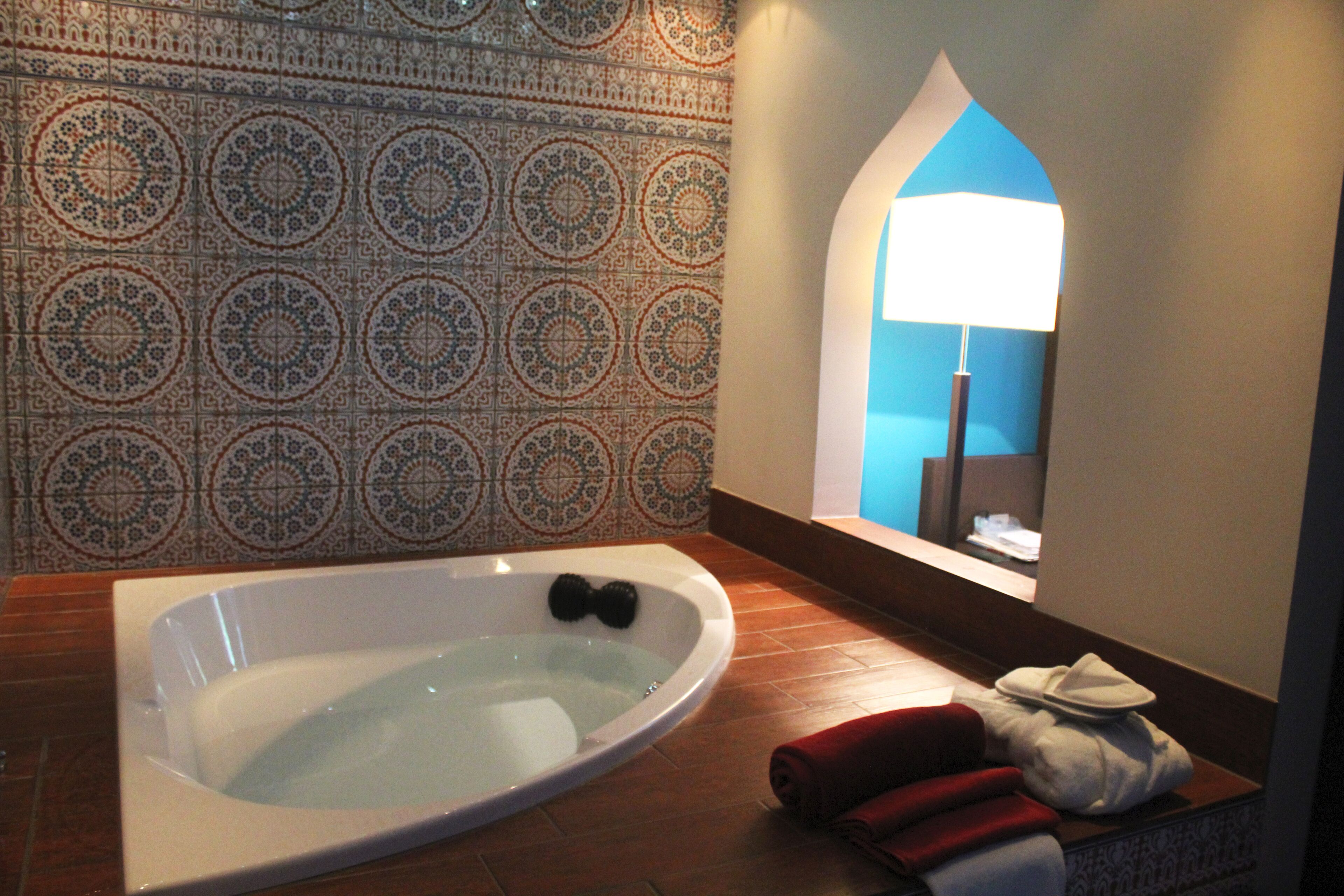 Un baño moderno con una bañera independiente, paredes con azulejos estampados y vistas a la ciudad a través de un ventanal.
