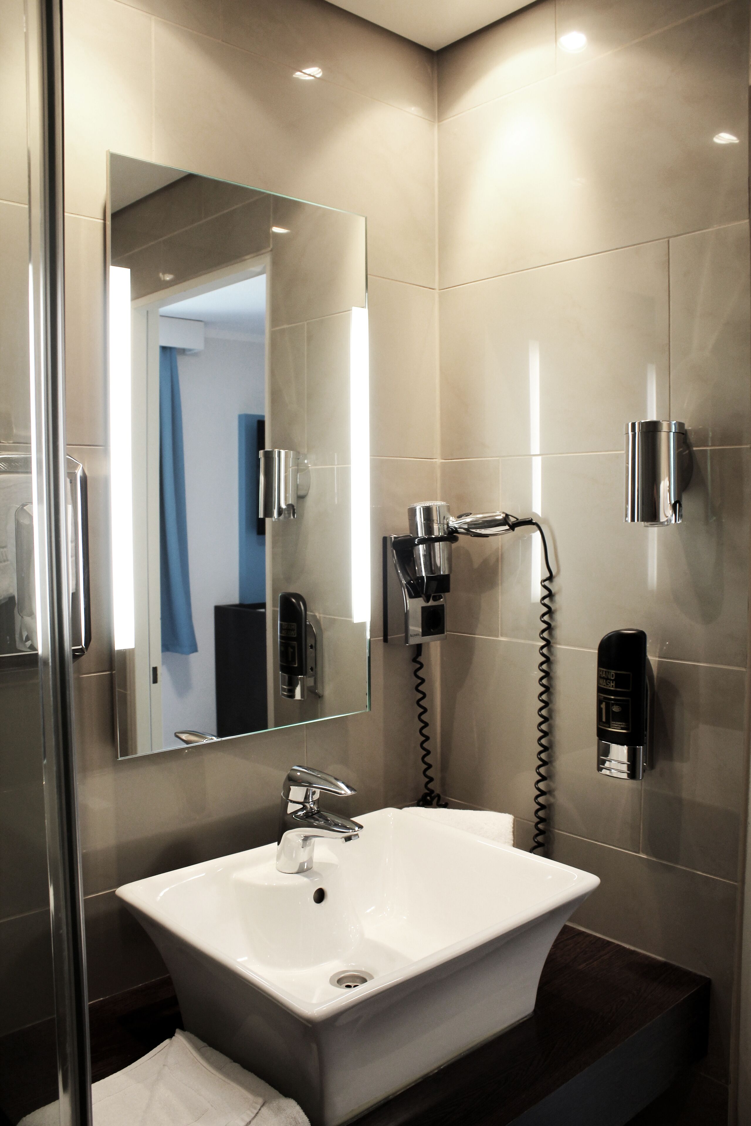 Un bagno moderno con un ampio specchio, un lavandino bianco e una cabina doccia in vetro.