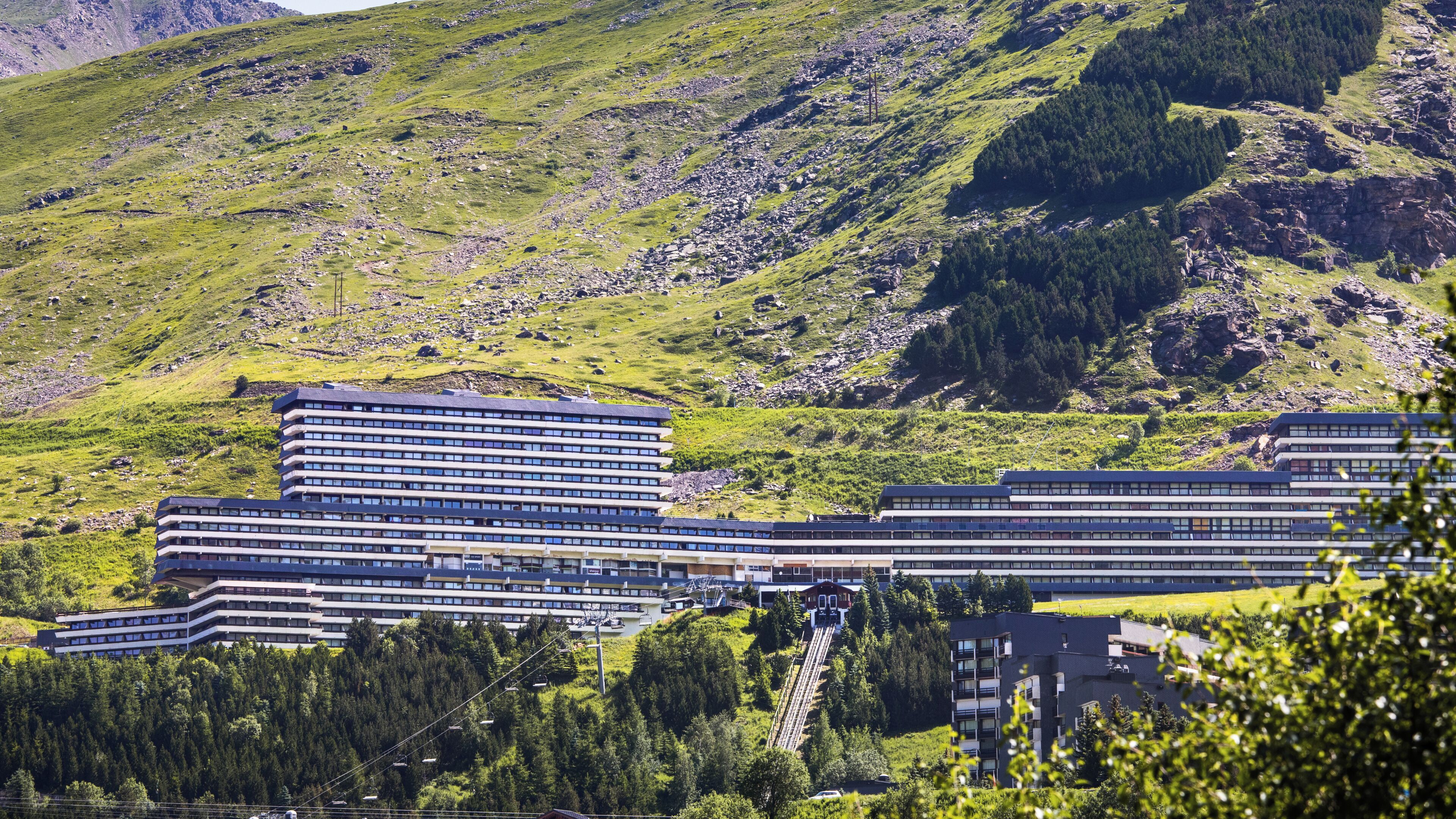 Un hotel moderno con diversi piani, una seggiovia e montagne sullo sfondo.