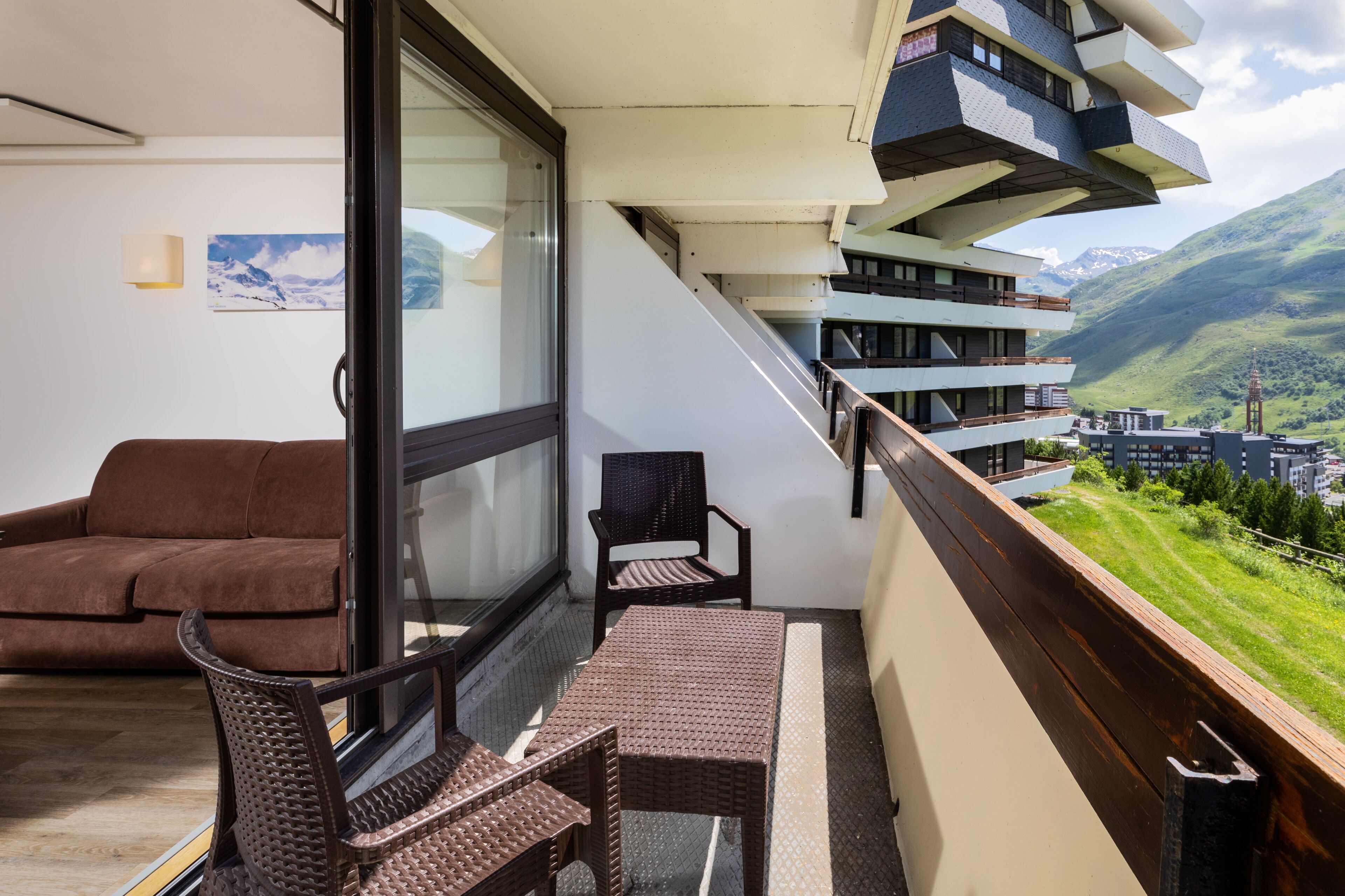 A balcony with a sofa, a chair, and a table. There is a view of a mountainous landscape.