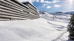 A modern hotel with a sloped roof, large windows, and a ski slope in the background. - SOWELL RÉSIDENCES Crêt Voland (Les Belleville)
