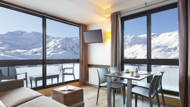 A modern hotel room with a balcony, a dining area, and a TV mounted on the wall. - SOWELL RÉSIDENCES Crêt Voland (Les Belleville)