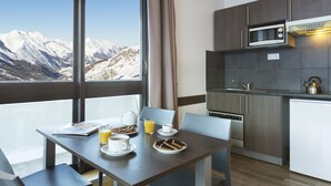 A modern kitchen with a view of snow-capped mountains, a dining table with breakfast items, and a built-in microwave. - SOWELL RÉSIDENCES Crêt Voland (Les Belleville)