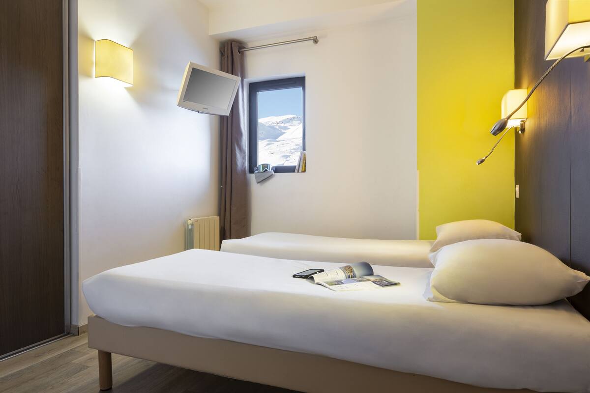 Hotellihuone, jossa on kaksi sänkyä, seinälle asennettu televisio ja ikkuna, josta avautuu näkymä lumihuippuisiin vuoriin.