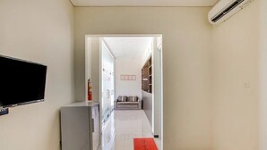 A hallway with a flat-screen TV, a refrigerator, and a red mat leading to a living area with a sofa and a TV.