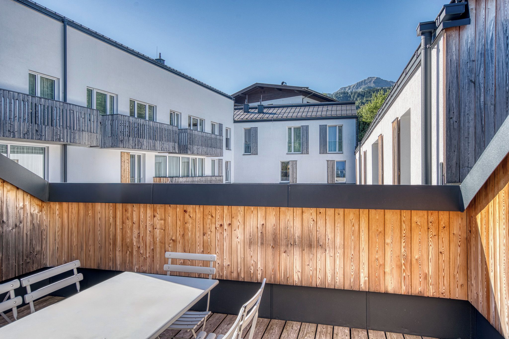 A modern outdoor patio with a wooden deck, a white table, and a bench.