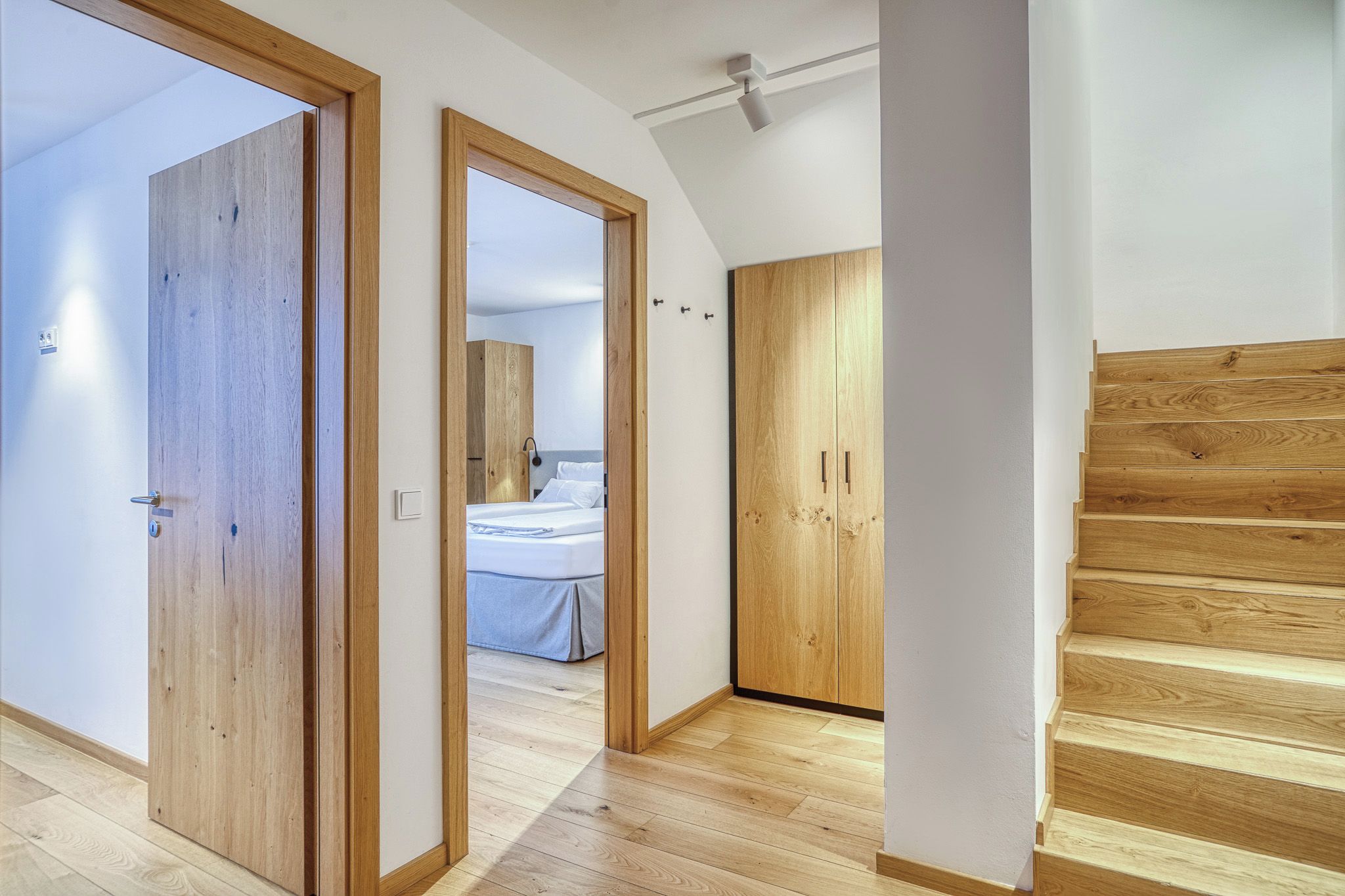 Un pasillo con puertas de madera que dan a un dormitorio con cama y armario.