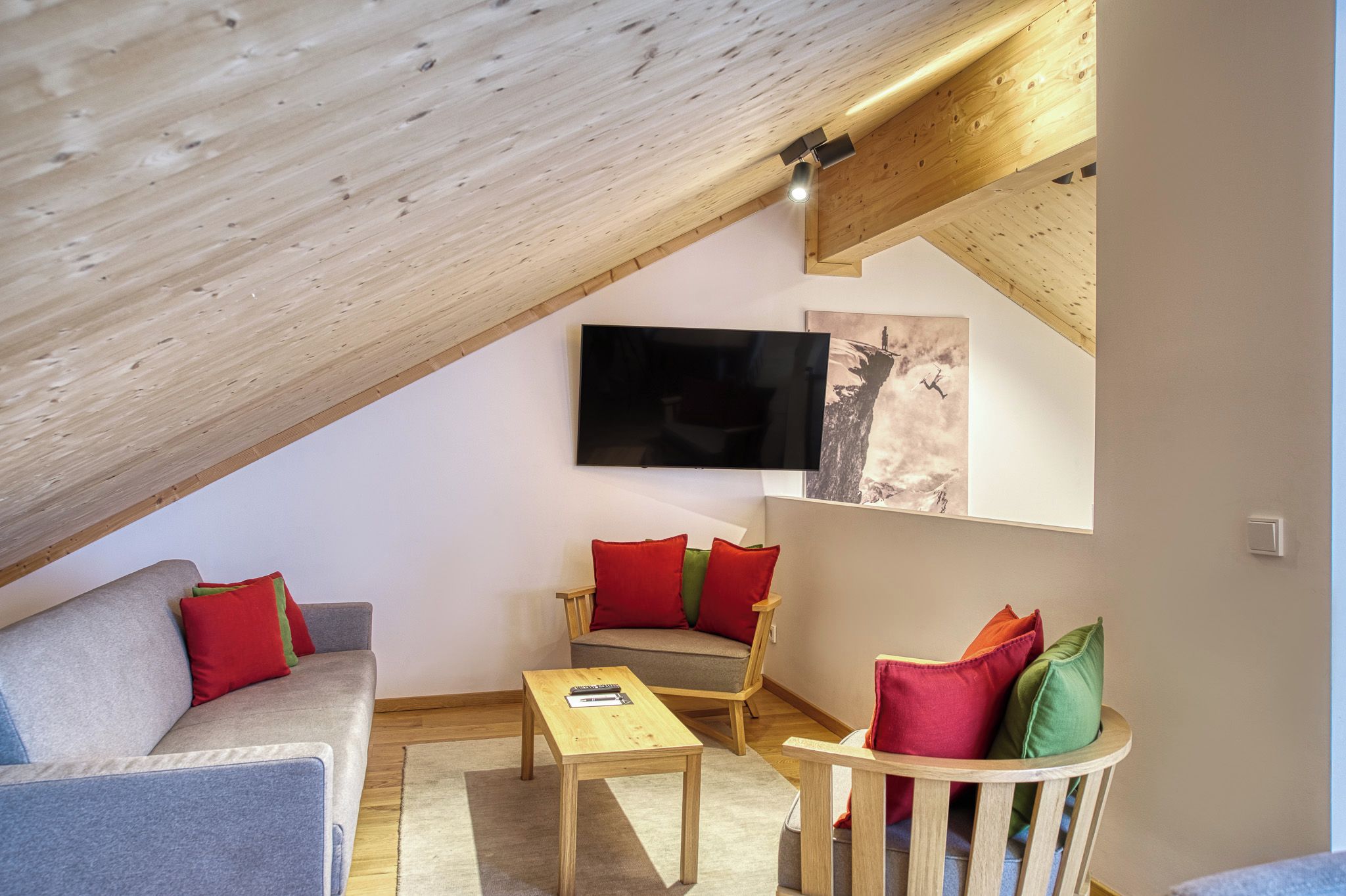A cozy loft-style living space with a sloped ceiling, a flat-screen TV, a sofa, a chair, and a small table.