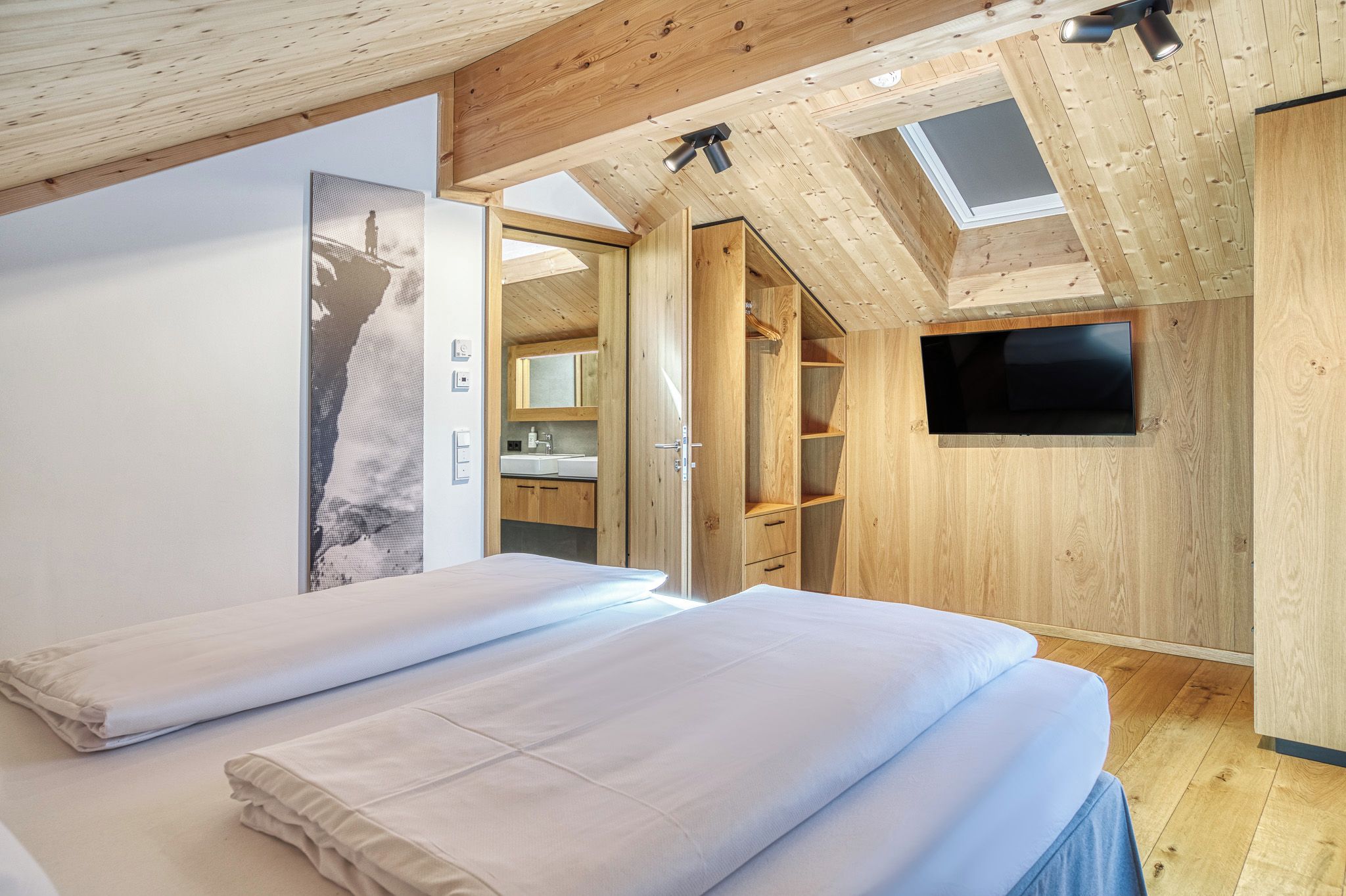 A bedroom with a bed, a TV, and a skylight.