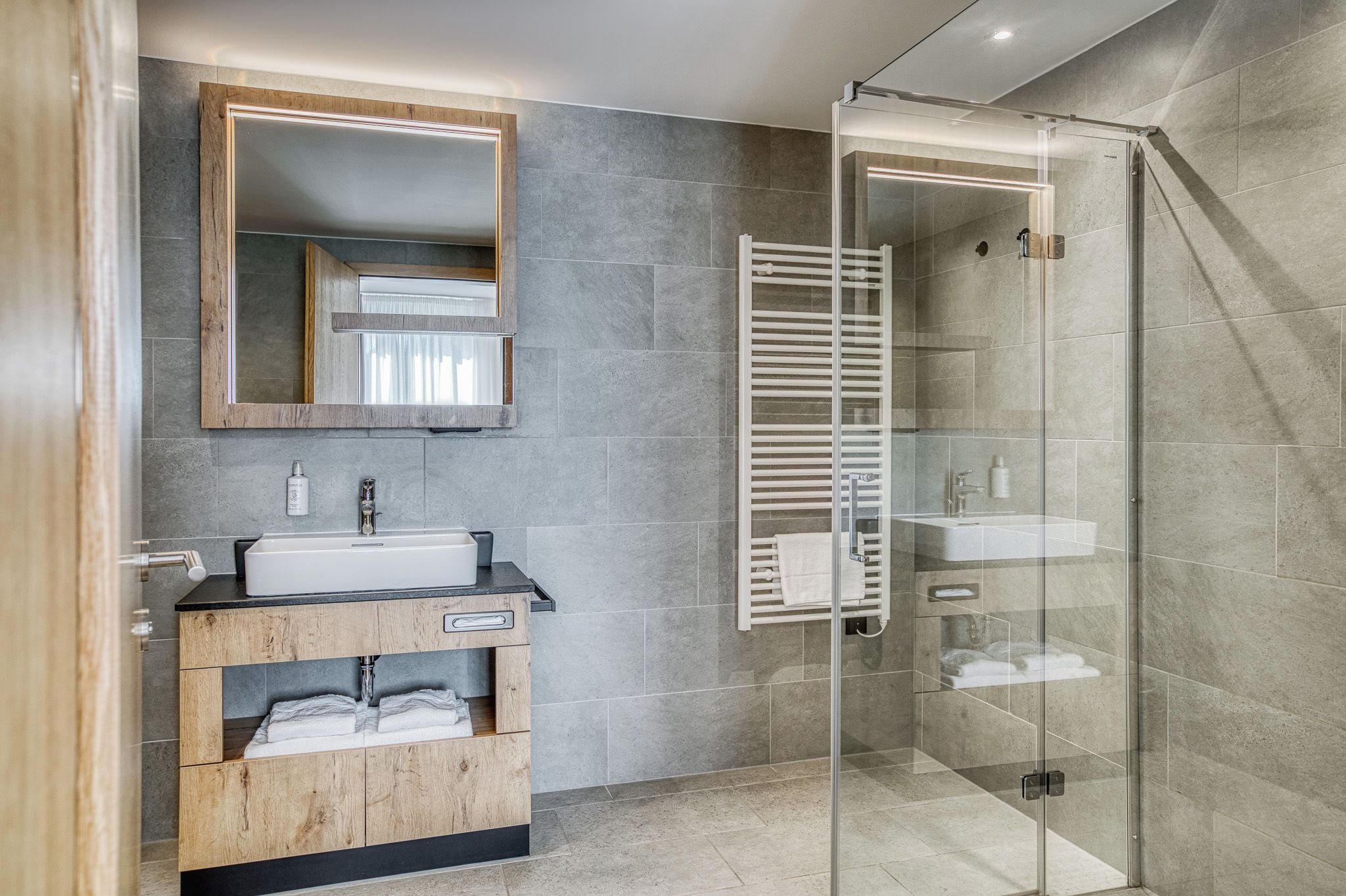 A modern bathroom with a glass shower enclosure, a wooden vanity with a sink, and a large mirror.