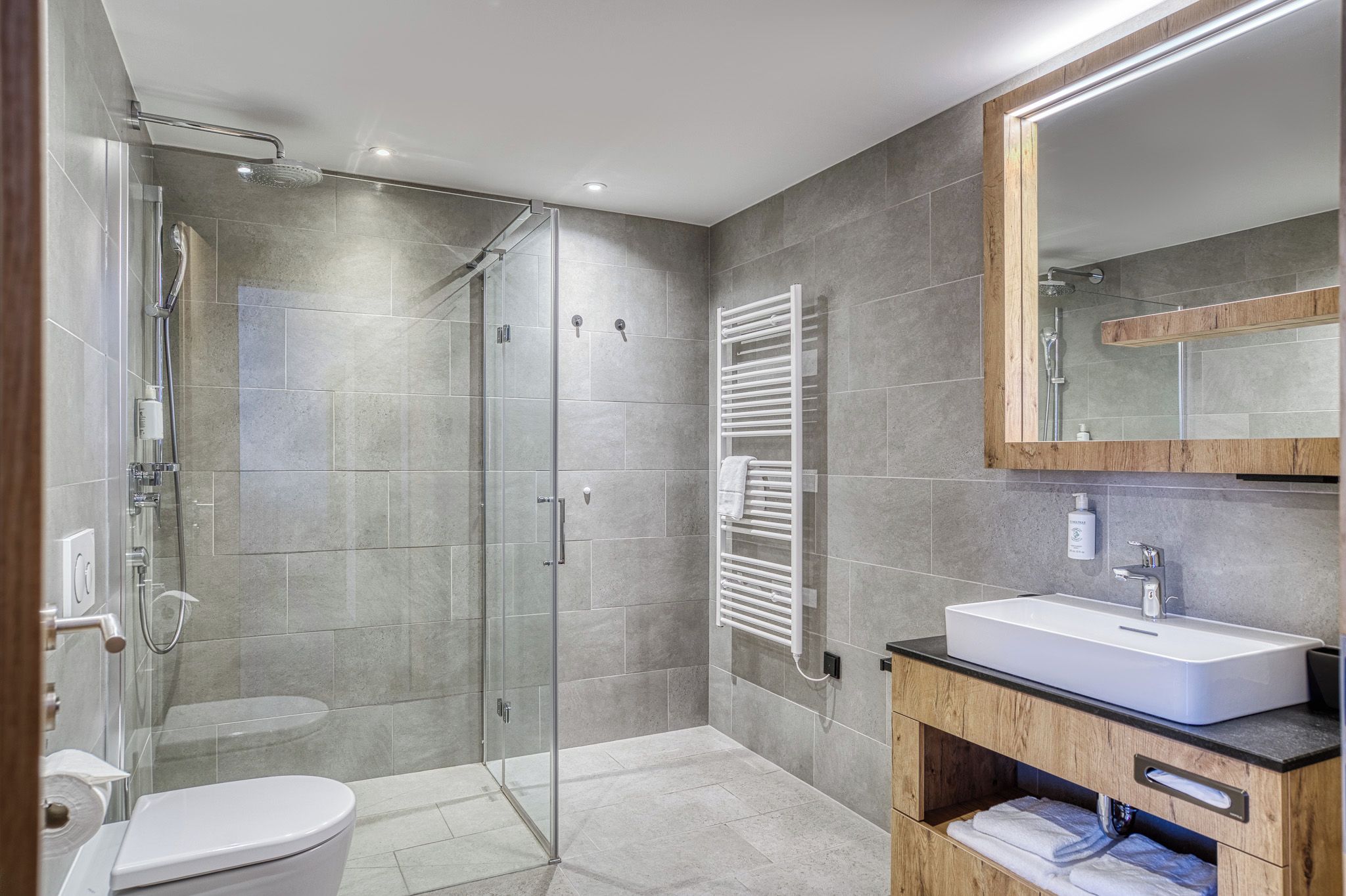 A modern bathroom with a glass-enclosed shower, a white toilet, and a wooden vanity with a sink.
