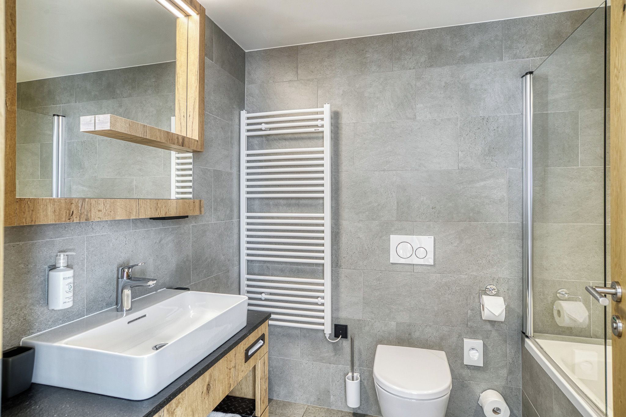 A modern bathroom with a large sink, mirror, towel rack, toilet, and shower.