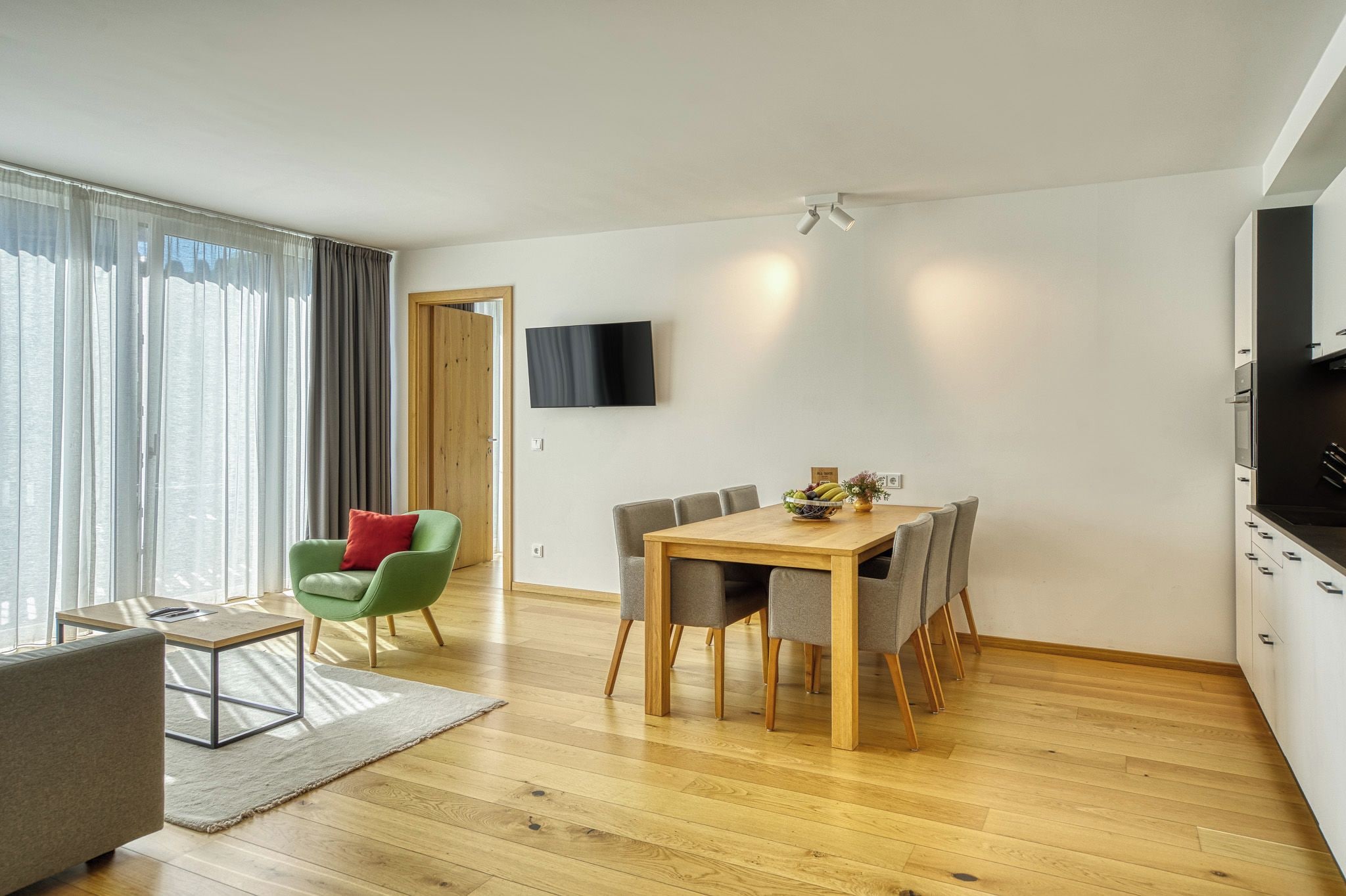 Un soggiorno moderno con zona pranzo, una TV a schermo piatto montata a parete e un tavolo da pranzo in legno con sedie.