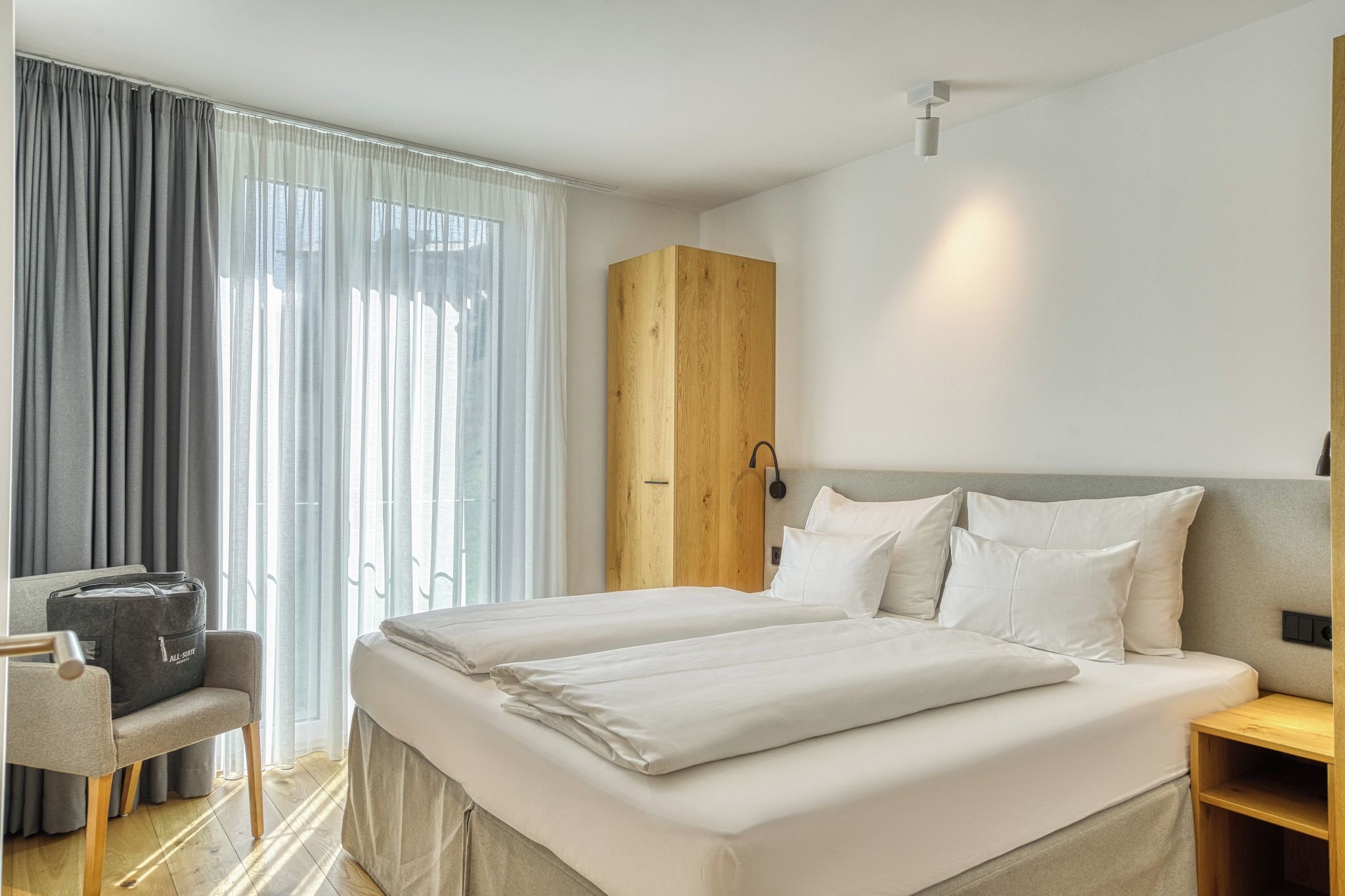 Una habitación de hotel con una cama, una silla, un armario y una mesita de noche.