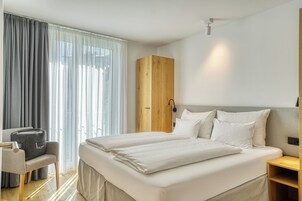 Una habitación de hotel con una cama, una silla, un armario y una mesita de noche.
