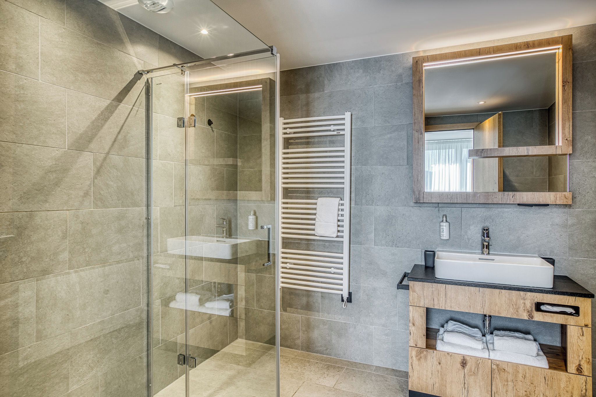 A modern bathroom with a glass shower enclosure, a built-in towel rack, and a wooden vanity with a sink.