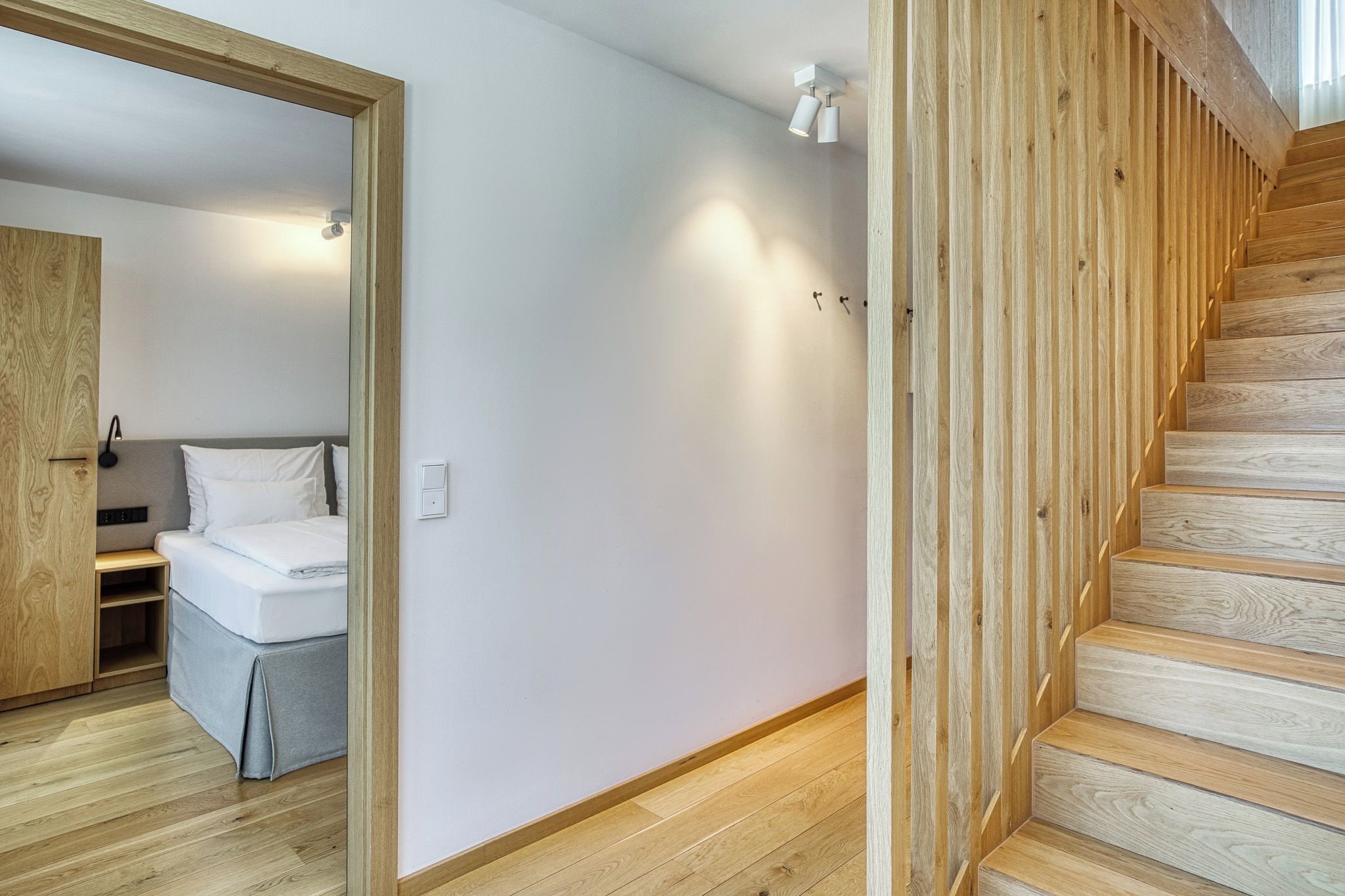 Un intérieur moderne avec un escalier en bois, un lit avec une literie blanche et un interrupteur sur le mur.