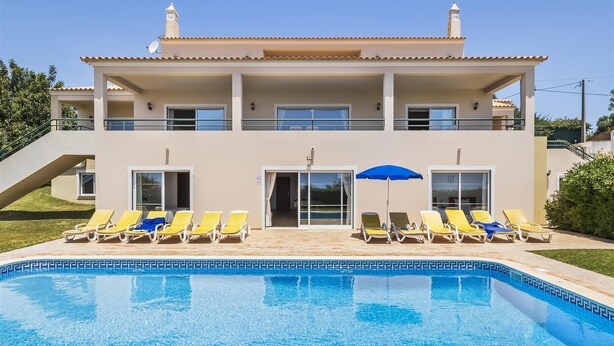 Um edifício de dois andares com piscina, várias varandas e espreguiçadeiras.