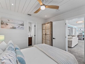 Una camera da letto con un letto, una ventola a soffitto, una porta con pannelli decorativi e vista su un'altra stanza.